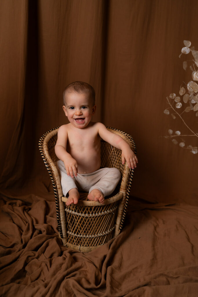 photographe professionnel Limoges -Bébé souriant qui est assis sur une chaise en rotin chez son photographe à Limoges